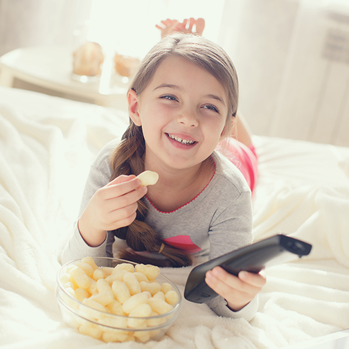 You girl laying on floor with remote in hand watching TV and eating popcorn