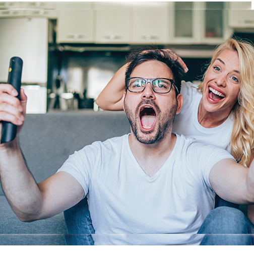 Young couple sitting on couch with remote in man's hand and excited about watching a sports program.