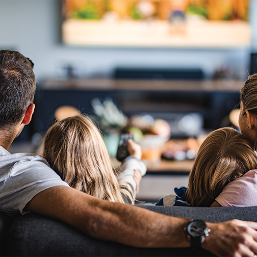 Rear view of a family sitting on a sofa watching TV.