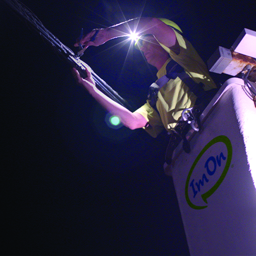 ImOn technician in bucket working on network fiber hanging from a pole at night.