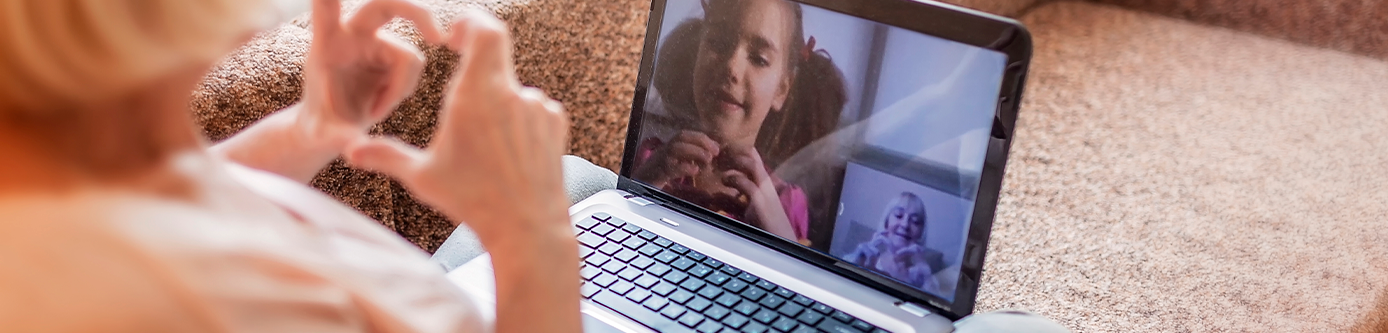 Grandma sitting on sofa video conferencing with grandchildren through laptop.