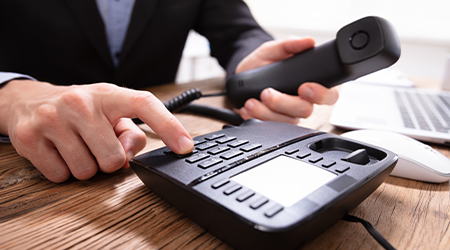 A businessman lifting the phone headset from his office phone and dialing.