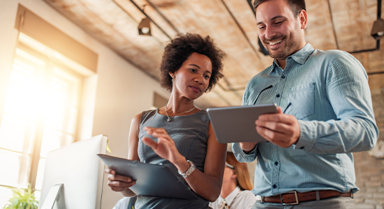 Two business colleagues walking in office while holding tablet and discussing a project.