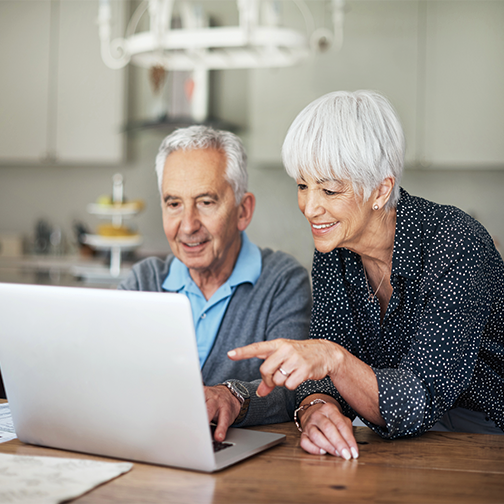 Older couple at kitchen table looking at their laptop.