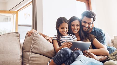 Mother, father and daughter sitting on couch using tablet device together.