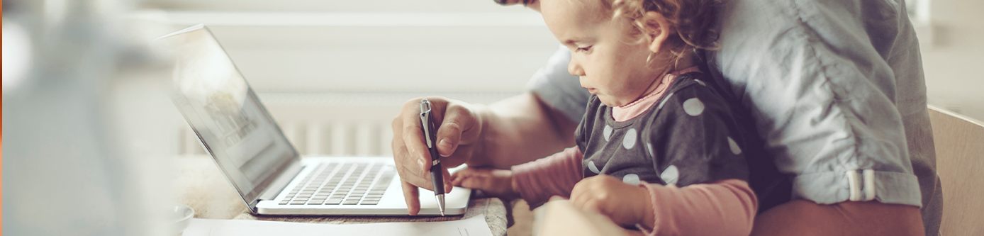 Father and daughter sitting at kitchen table looking at laptop.